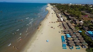A beach with a row of thatched umbrellas and lounge chairs, a sandy shore, and a clear view of the ocean. - An Bang Garden Homestay (Da Nang)