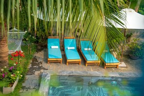 A poolside area with lounge chairs and a small garden. - An Bang Garden Homestay (Da Nang)