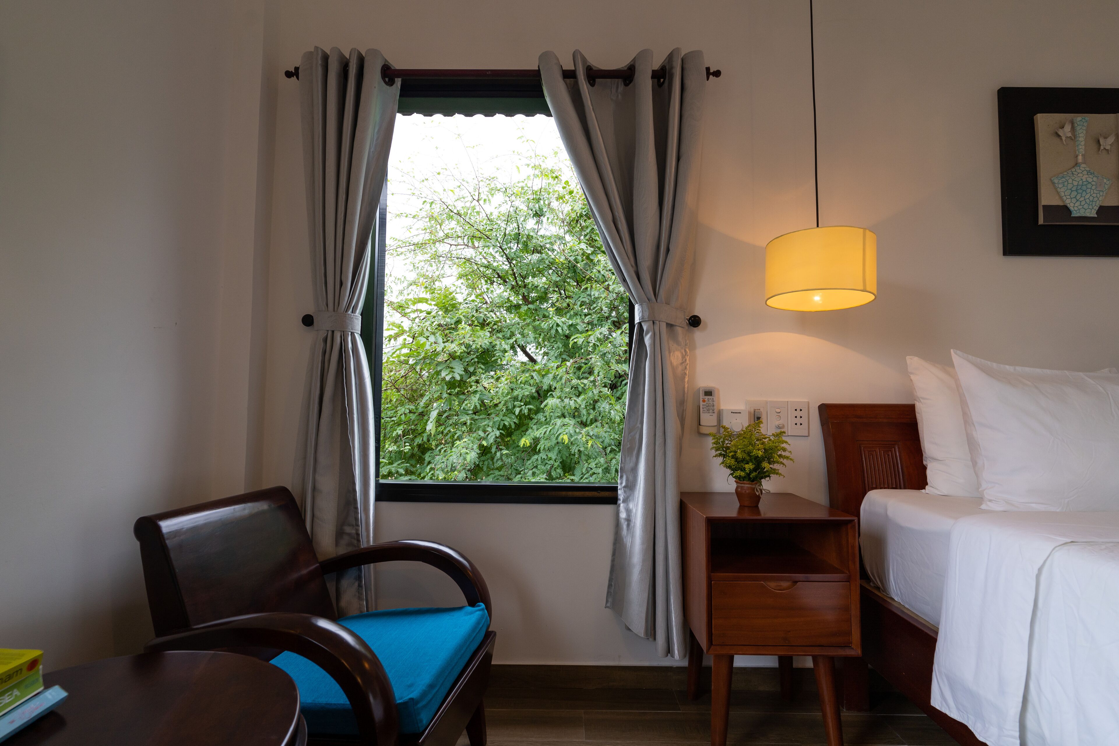 Een hotelkamer met een bed, een stoel, een nachtkastje met een lamp en een raam met gordijnen.