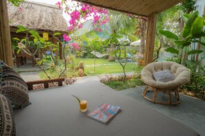 A cozy outdoor seating area with a cushioned chair, a magazine, and a drink on a table. - An Bang Garden Homestay (Da Nang)