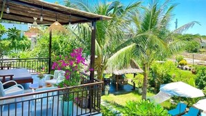 A covered outdoor seating area with tables and chairs, surrounded by lush greenery and palm trees. - An Bang Garden Homestay (Da Nang)