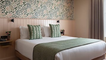 Una cama bien hecha con una colcha y almohadas de diseño verde y blanco, un cabecero de madera, una mesita de noche con un florero y una ventana grande con cortinas.