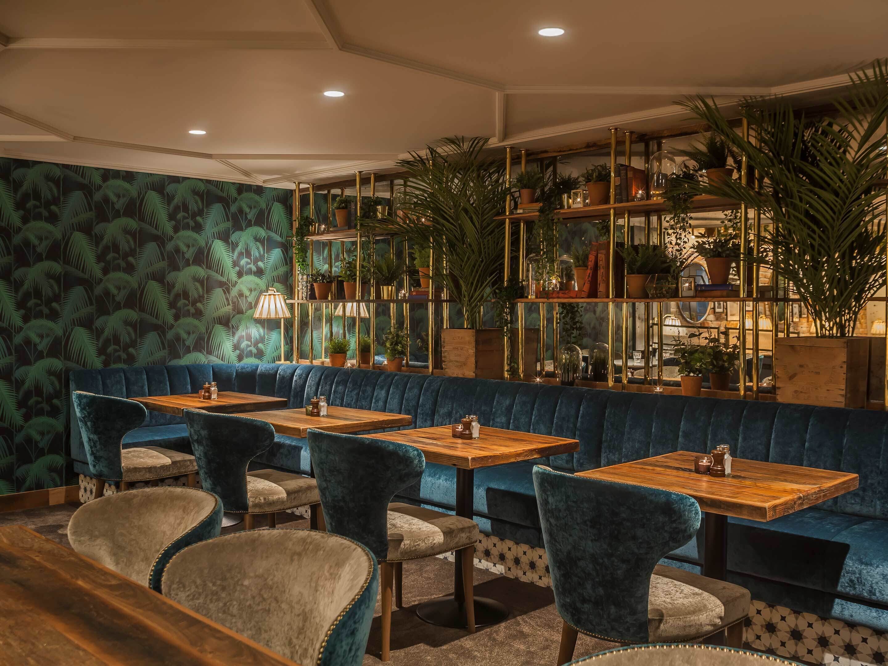 A cozy restaurant with plush seating, wooden tables, and a green patterned wall.