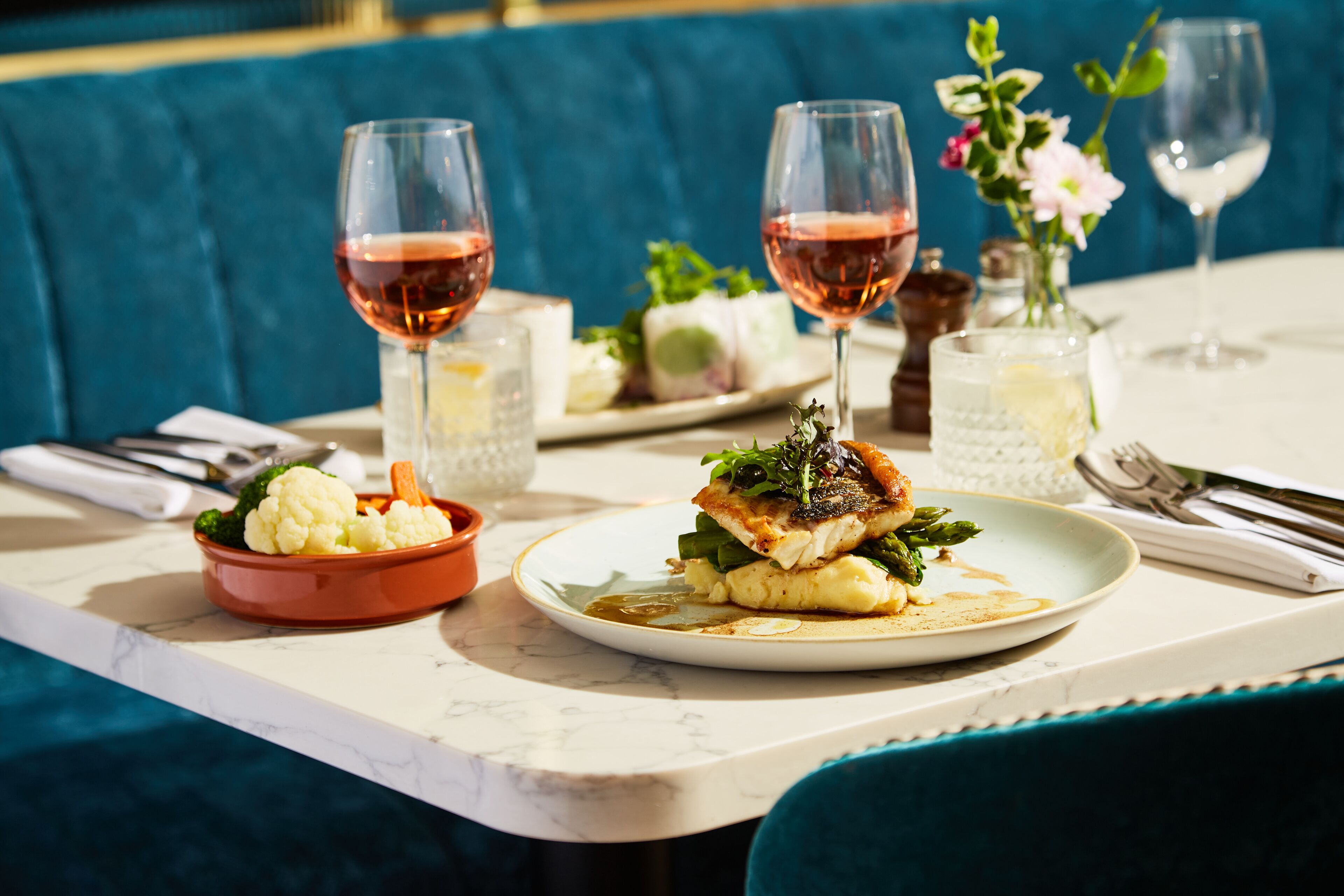 A dining table with plates of food, glasses of wine, and a vase with flowers.