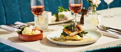 A dining table with plates of food, glasses of wine, and a vase with flowers.