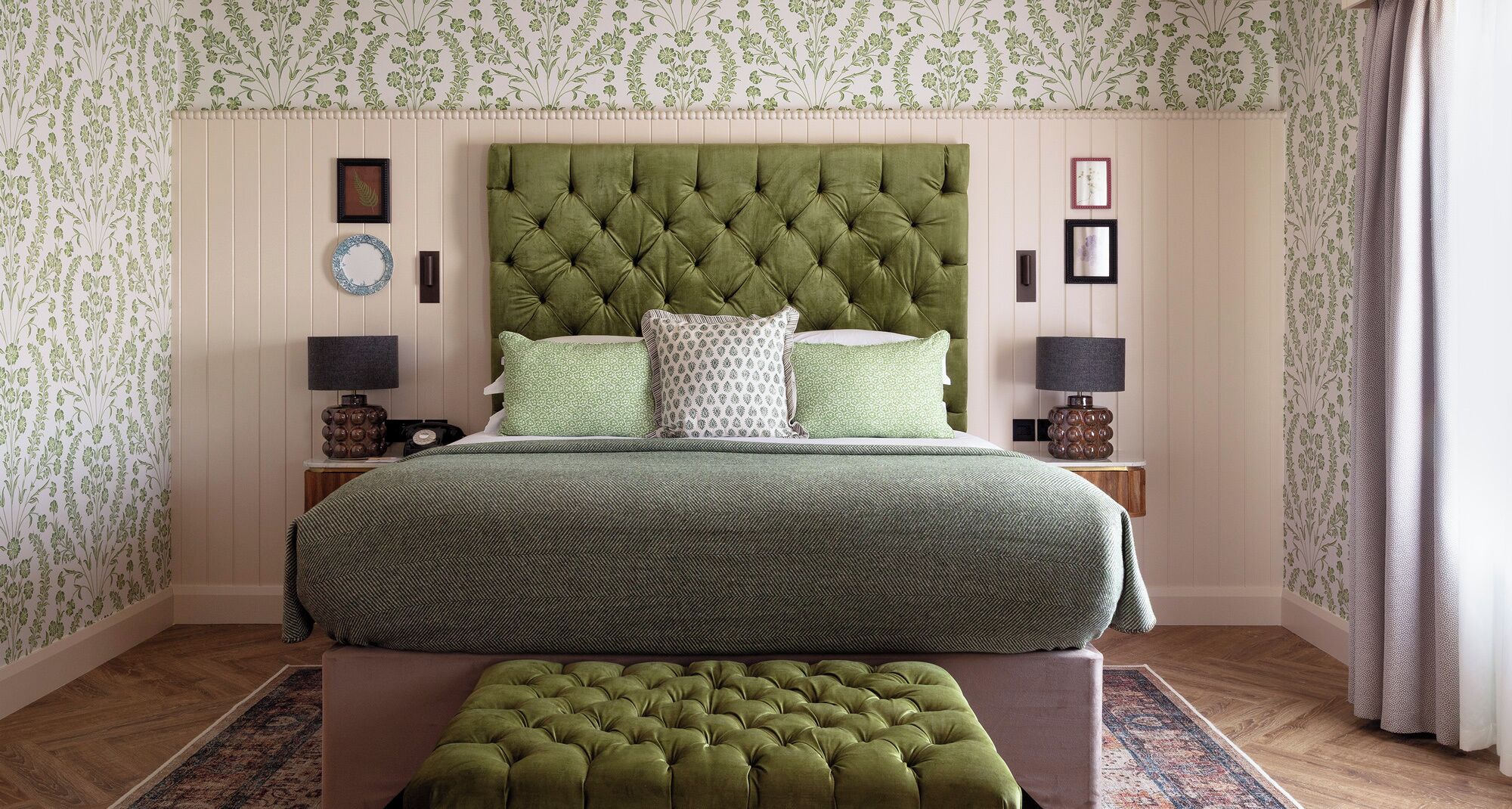 A bedroom with a tufted headboard, green bedding, two bedside tables with lamps, and a patterned rug.