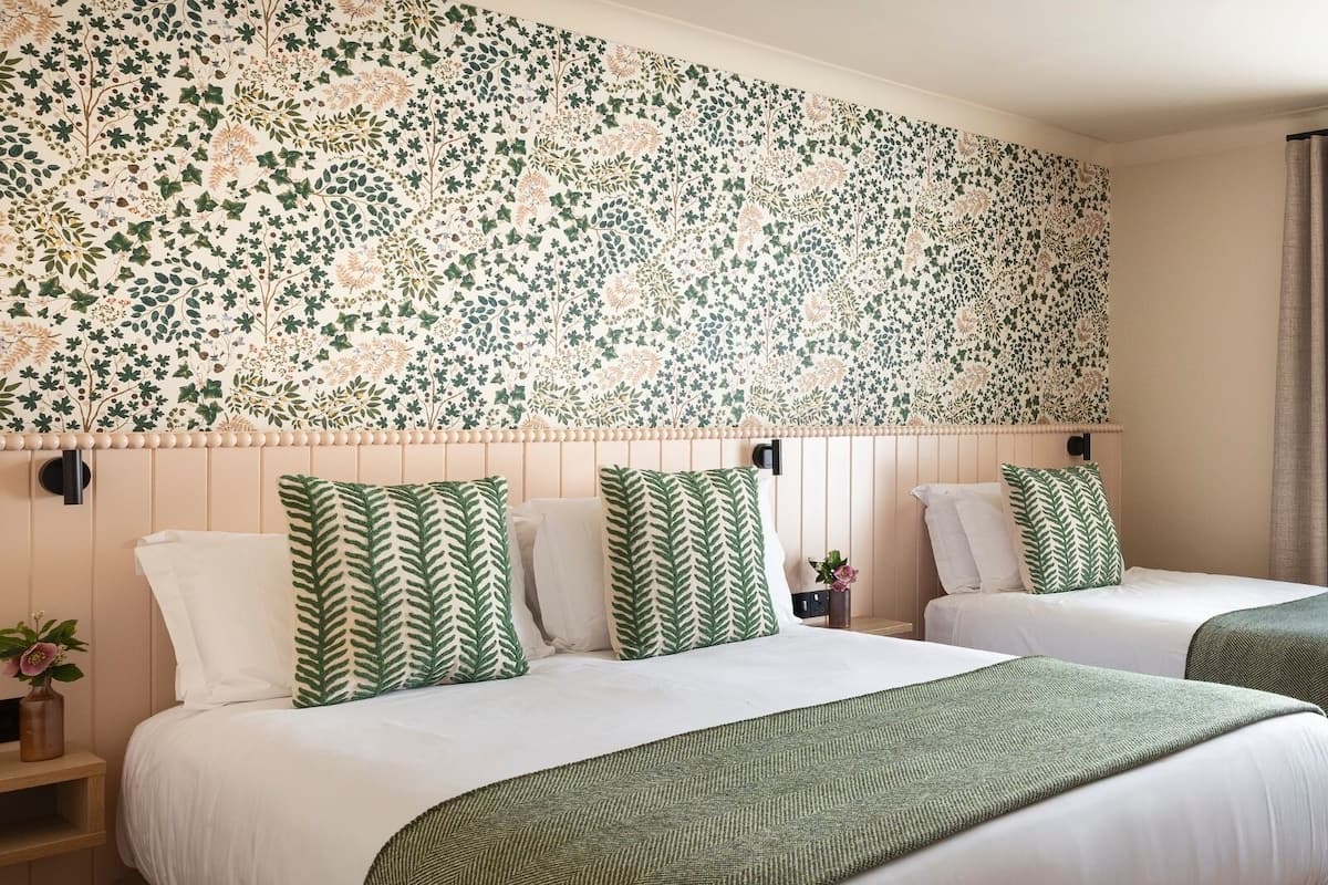 Une chambre d’hôtel avec deux lits, chacun agrémenté de draps verts et blancs, et un papier peint à motifs floraux.