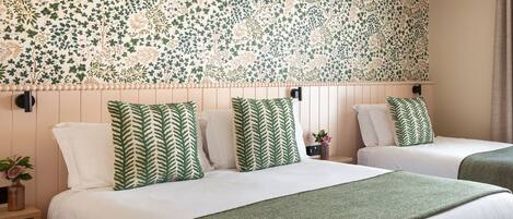 A hotel room with two beds, each with green and white bedding, and a floral-patterned wallpaper.