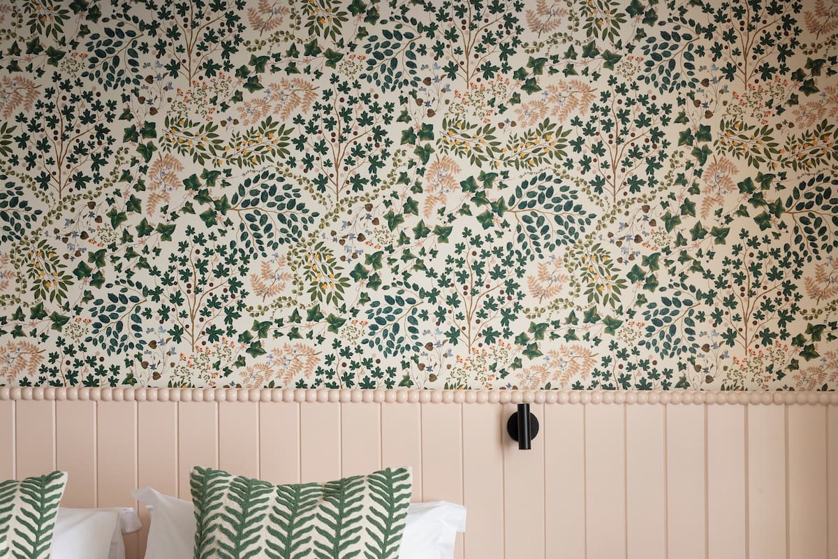 Une chambre à coucher avec un lit, des oreillers, une table de chevet et un mur orné d’un motif floral.