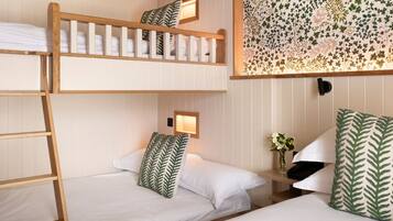 Een slaapkamer met een stapelbed, witte beddengoed, een ladder en bloemenbehang.