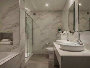 A modern bathroom with marble walls, a glass shower enclosure, a toilet, and two sinks with faucets. - The Ashe Hotel (Tralee)