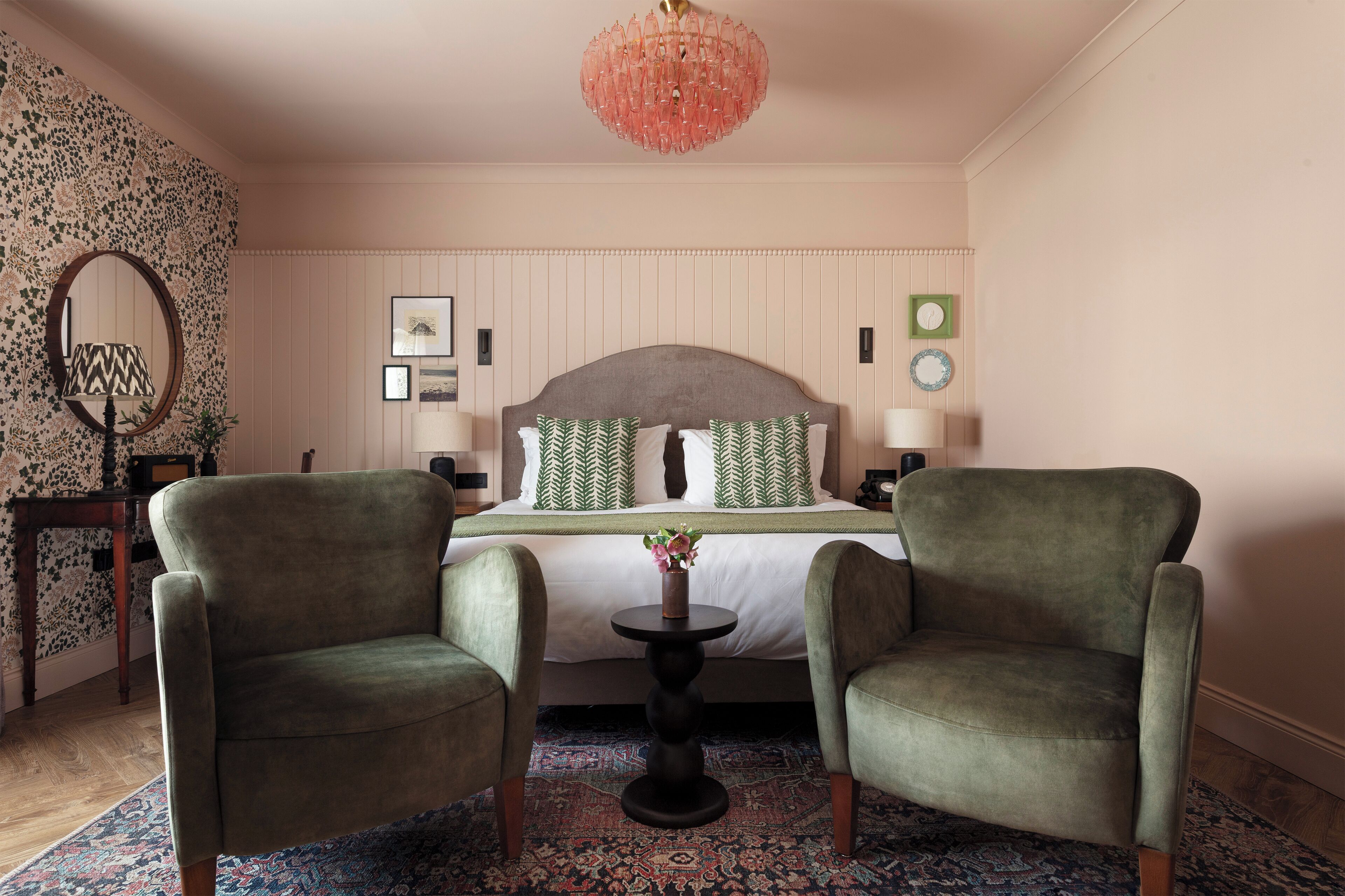 A hotel room with a bed, two armchairs, a small table, a patterned rug, and a decorative chandelier.