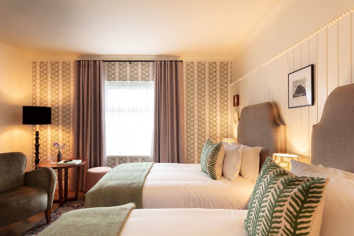 Une chambre d’hôtel avec deux lits, une télévision, une petite table avec une lampe et une fenêtre avec des rideaux.