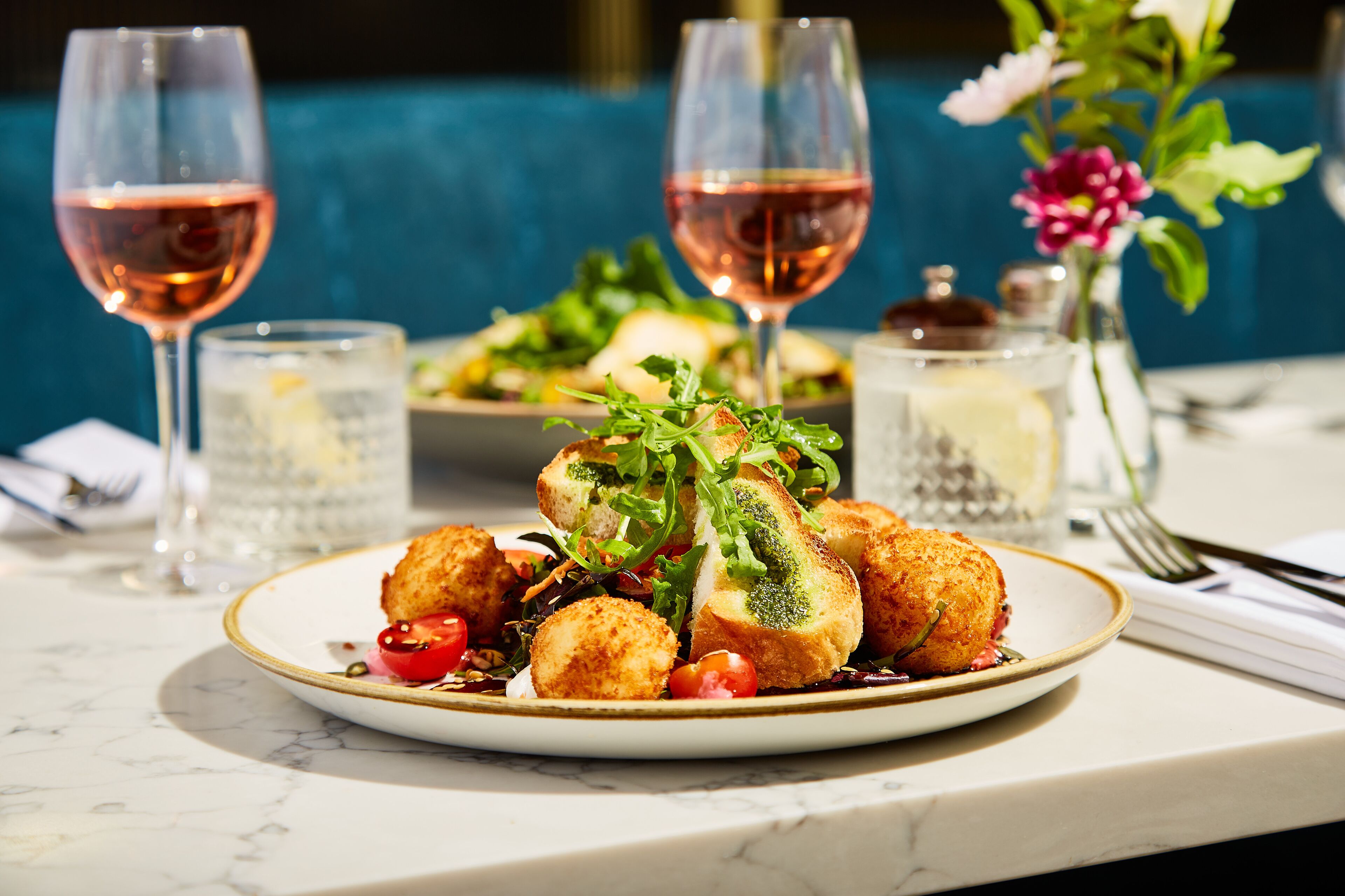 A dining table with a plate of food, two glasses of wine, and a vase with flowers.