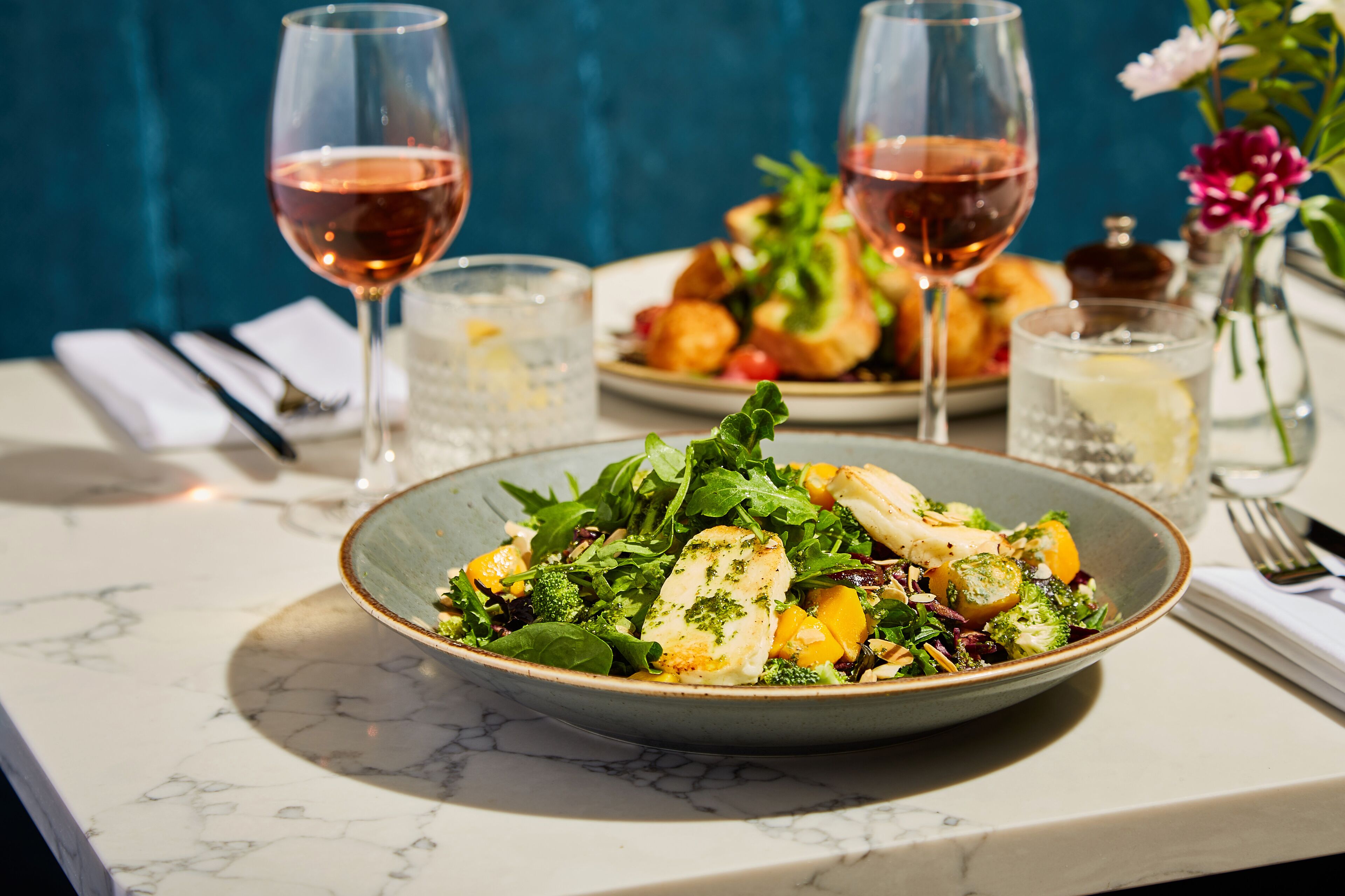 A dining table with a bowl of salad, two glasses of wine, and a vase with flowers.