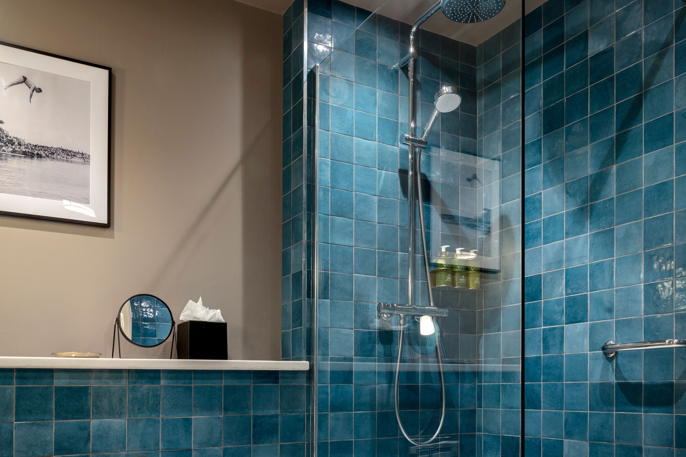Un baño con azulejos azules, un cuadro en la pared, un espejo redondo y un perchero para toallas.