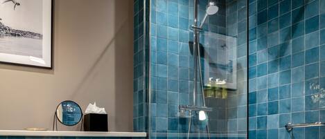 Un baño con azulejos azules, un cuadro en la pared, un espejo redondo y un perchero para toallas.