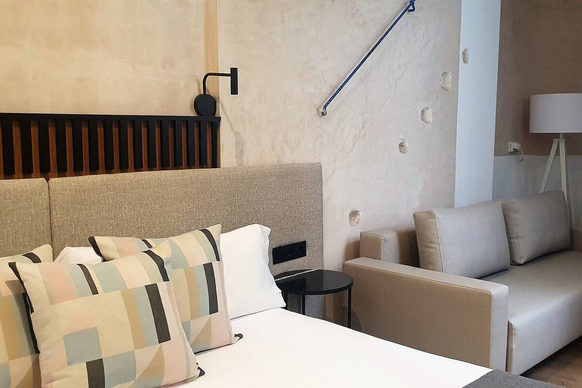 Una habitación de hotel moderna con una cama, un sofá, una mesita y una lámpara.