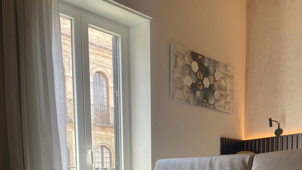 A living room with a sofa, a round table, a window with curtains, and a wall-mounted light fixture. - ISA SEVILLA Suites (Seville)