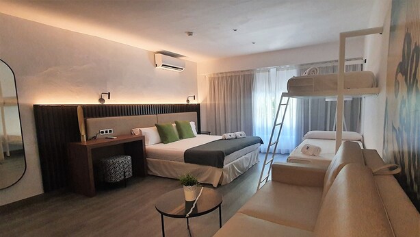 Una habitación de hotel moderna con una cama grande, un sofá, una mesita y una escalera para acceder a la cama superior.