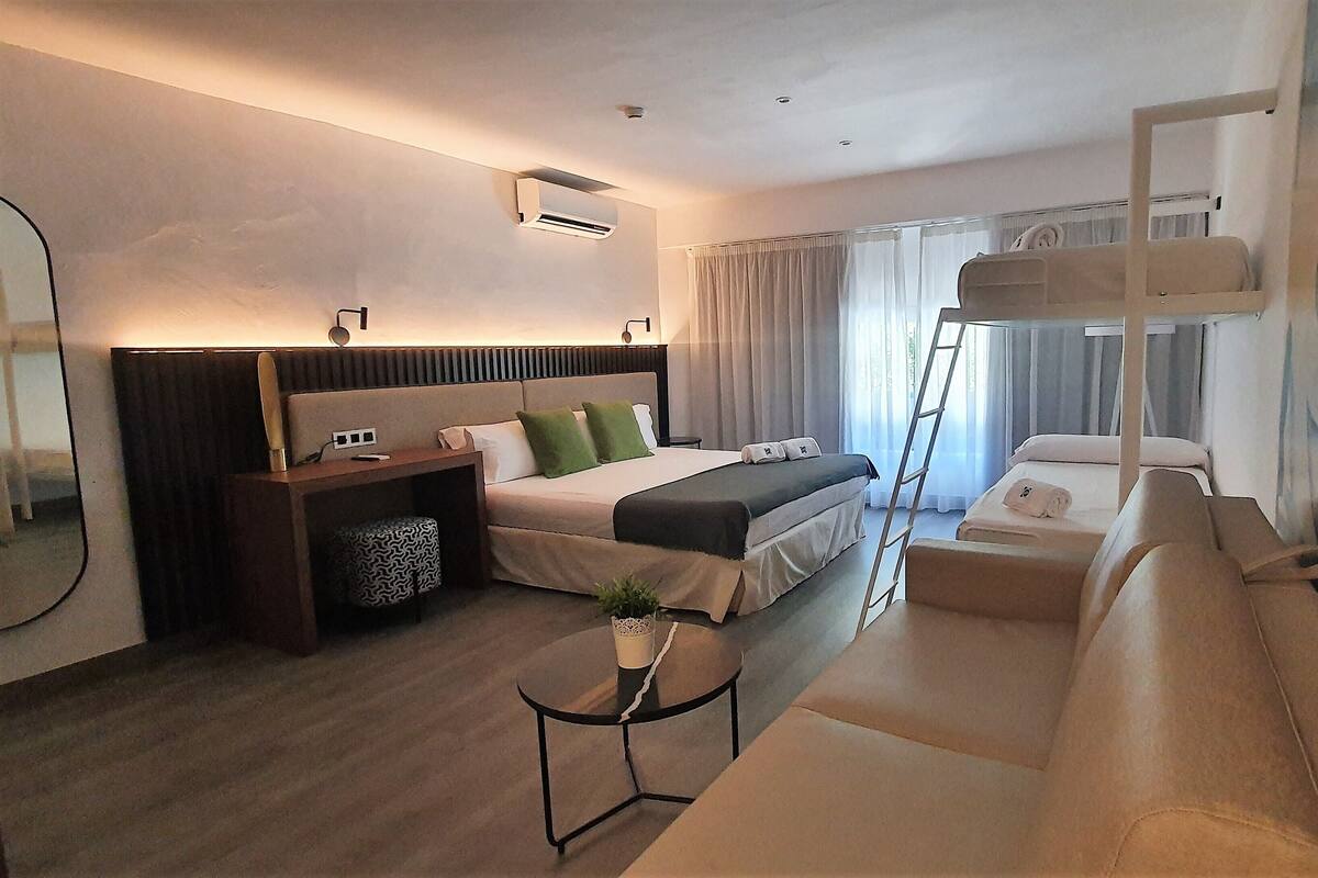 Una habitación de hotel moderna con una cama grande, un sofá, una mesita y una escalera para acceder a la cama superior.