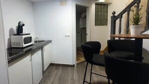 Una cocina compacta con microondas, pileta y sillas negras. Se observa una escalera con una planta en maceta al fondo.