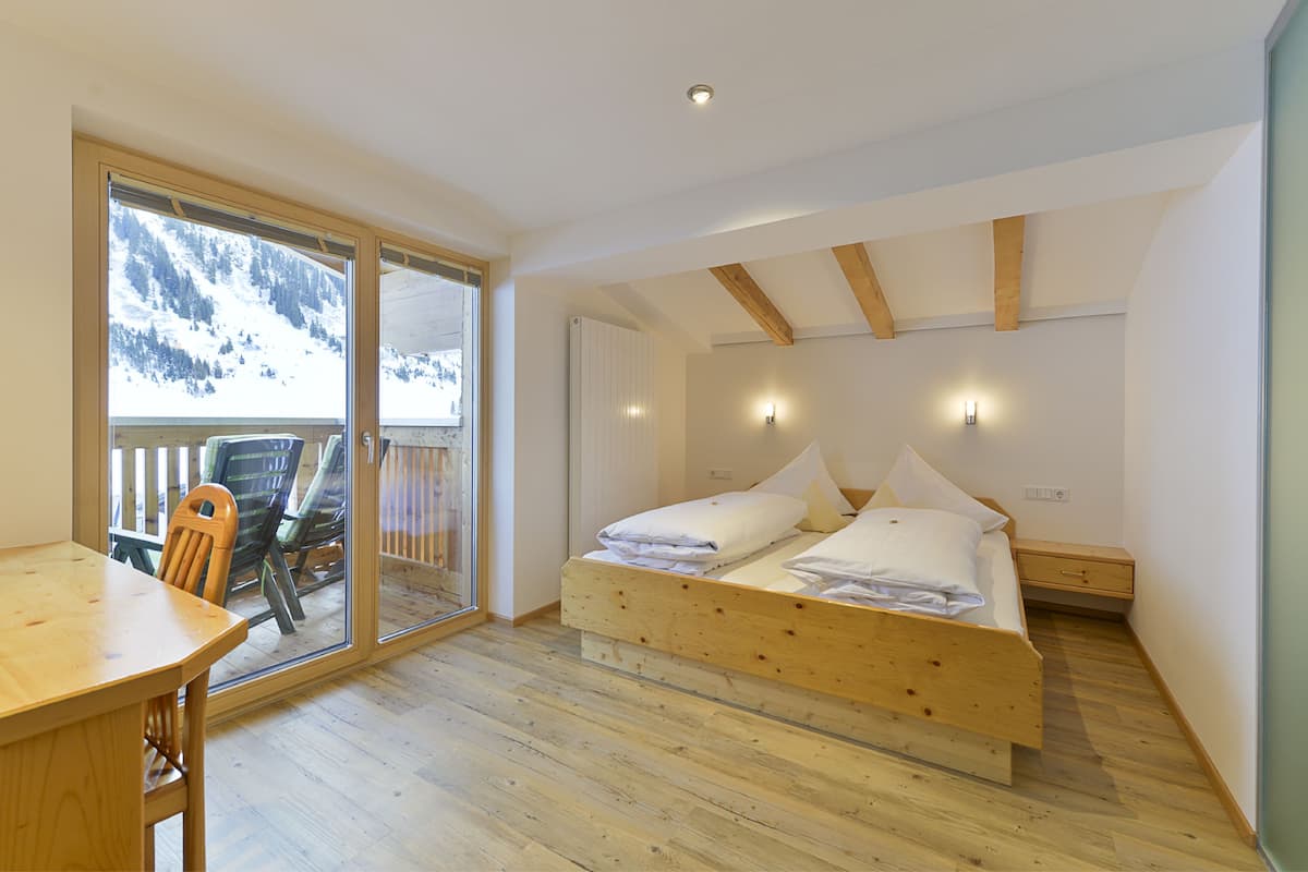 A bedroom with a wooden bed, a dining table, and a view of a snowy mountain through a sliding door.