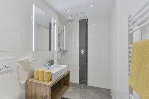 A modern bathroom with a white sink, wooden vanity, and a glass-enclosed shower area. - Pension Widderstein (Lech am Arlberg)