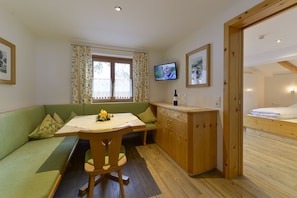 A cozy room with a green sofa, wooden dining table, and a TV mounted on the wall. - Pension Widderstein (Lech am Arlberg)