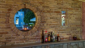 A brick wall with a circular mirror reflecting a building and a row of bottles on a ledge. - Villa Plumeria Flower (Chania)