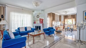 A spacious living room with blue sofas, a fireplace, and a chandelier. - Villa Plumeria Flower (Chania)