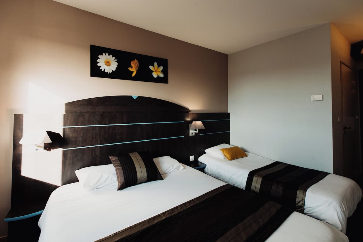 Une chambre d’hôtel avec deux lits, une tête de lit sombre, un tableau représentant des fleurs accroché au mur et une table de chevet avec une lampe.