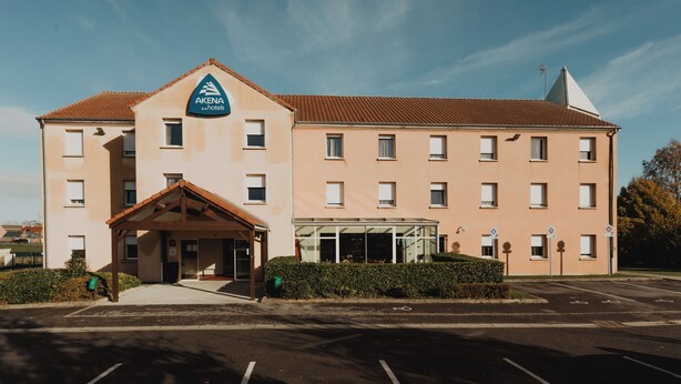 Ein mehrstöckiges Hotel mit einer markanten Eingangsparte, überdachter Wartezone und einem Parkplatz.