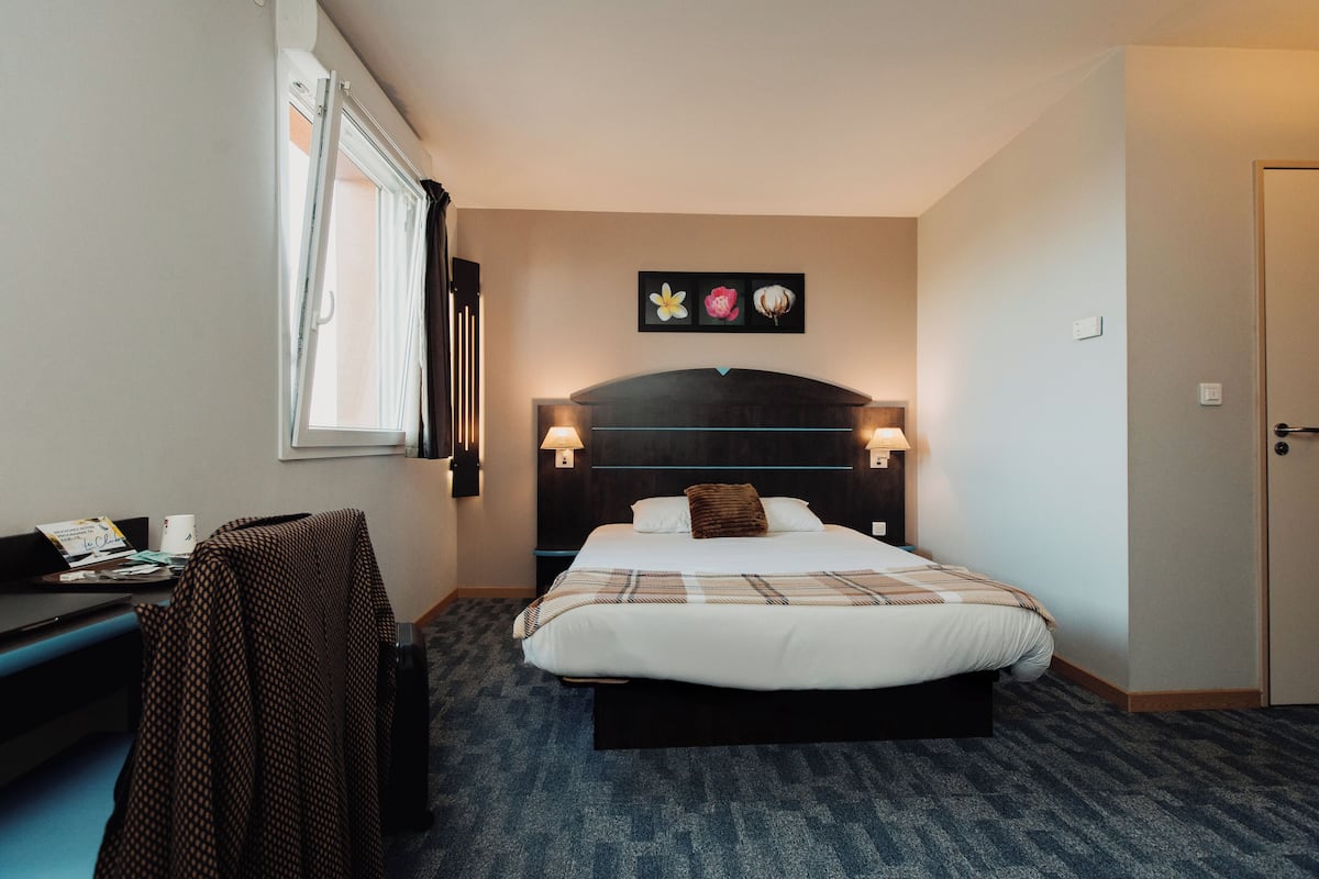 Une chambre d’hôtel avec un lit, des lampes de chevet, un bureau et une fenêtre.