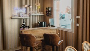 Zona de bar con paneles de madera, dos sillones de cuero, un letrero de neón y vistas al exterior.