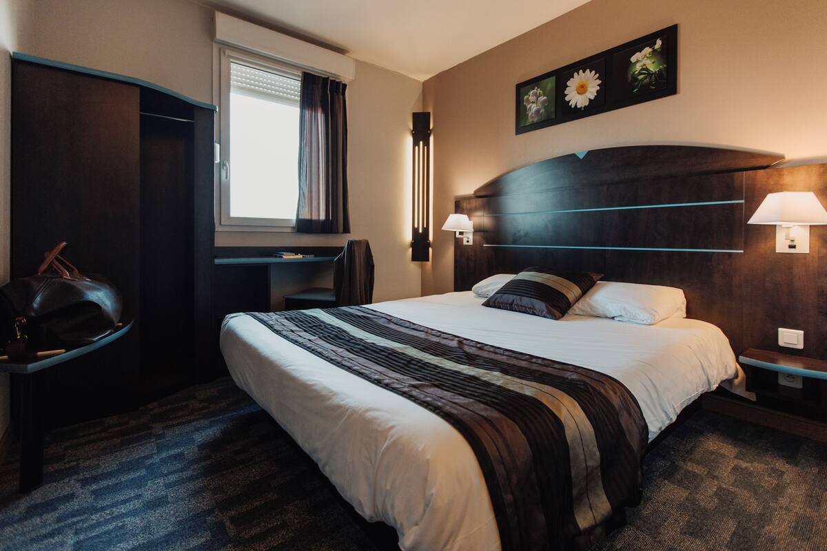 Une chambre d’hôtel avec un grand lit, un bureau, une chaise et une armoire.