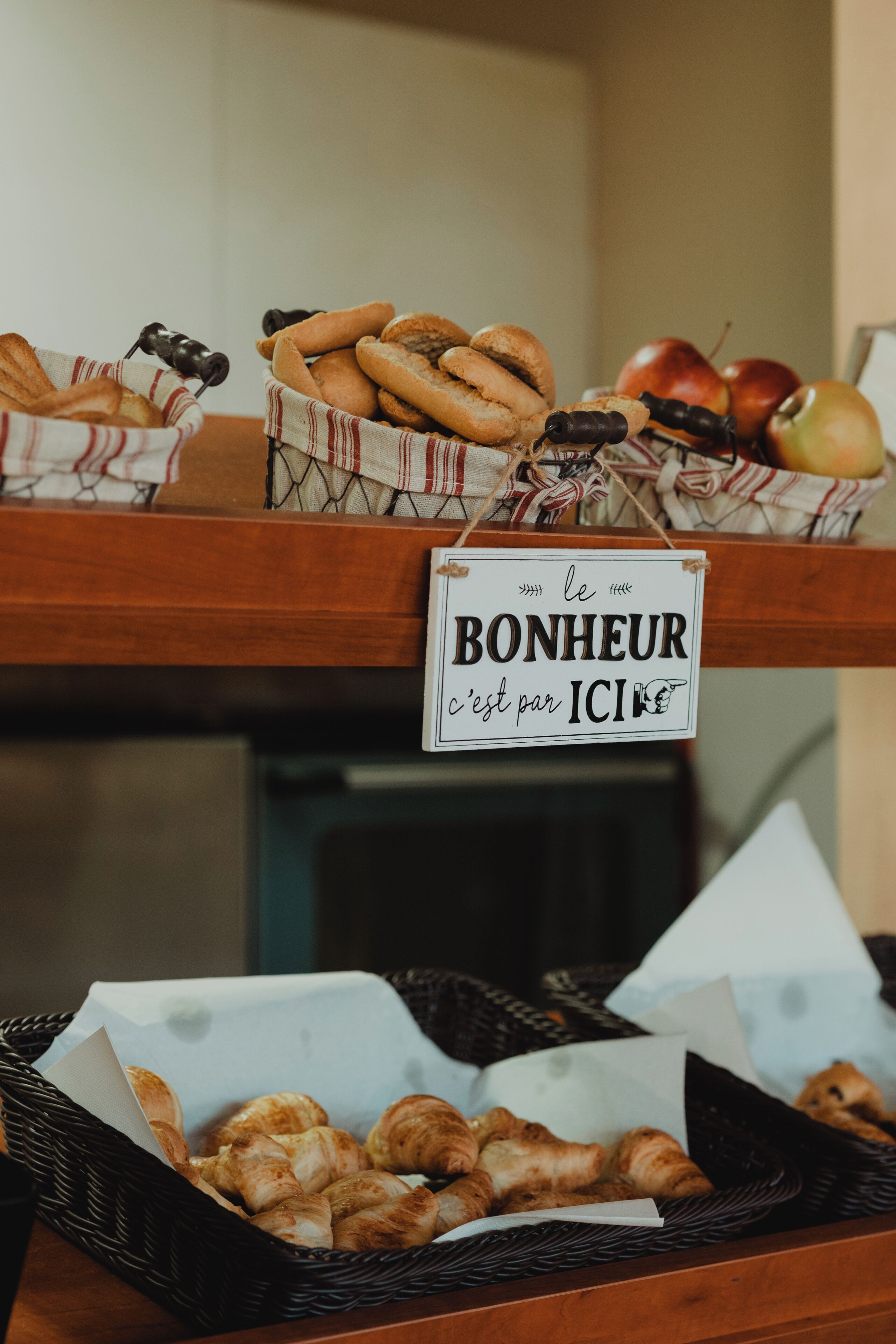 A buffet with various breads and pastries, including croissants and baguettes, displayed on wooden shelves.