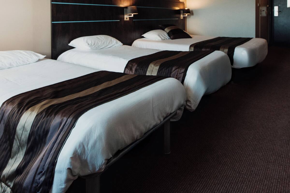 Une chambre d’hôtel avec trois lits, des têtes de lit sombres et un sol recouvert de moquette.
