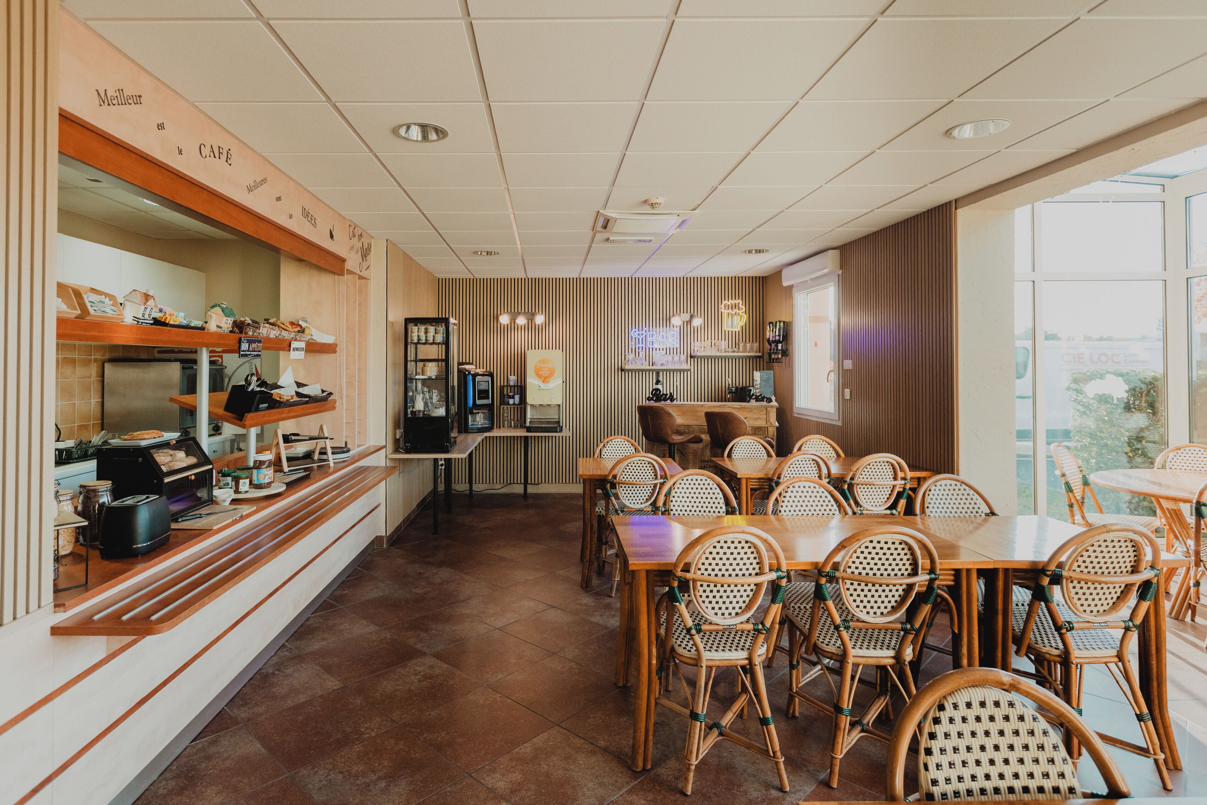 A café with a long counter, wicker chairs, and a tiled floor.