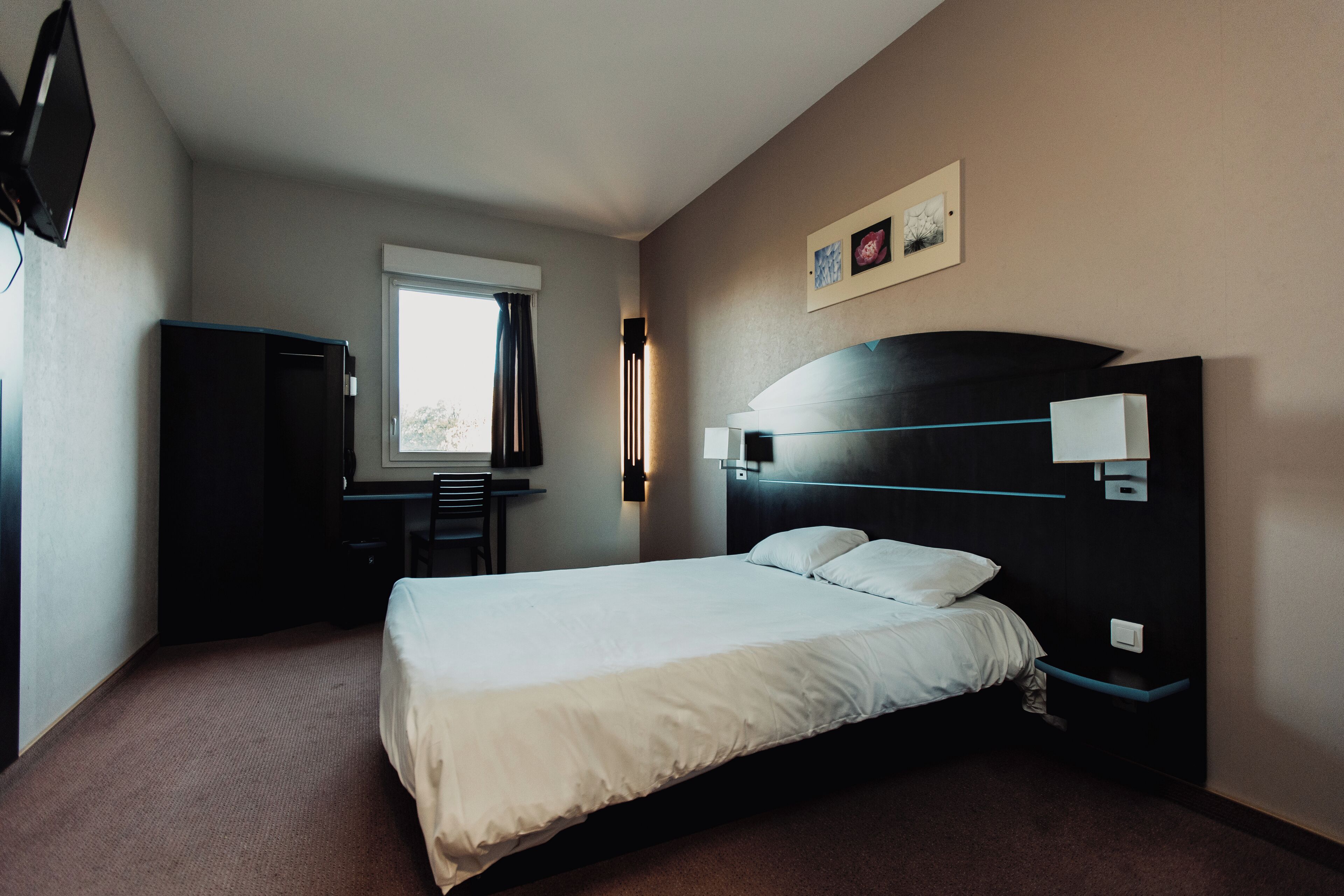 A hotel room with a bed, a desk, a chair, a TV, and a window.