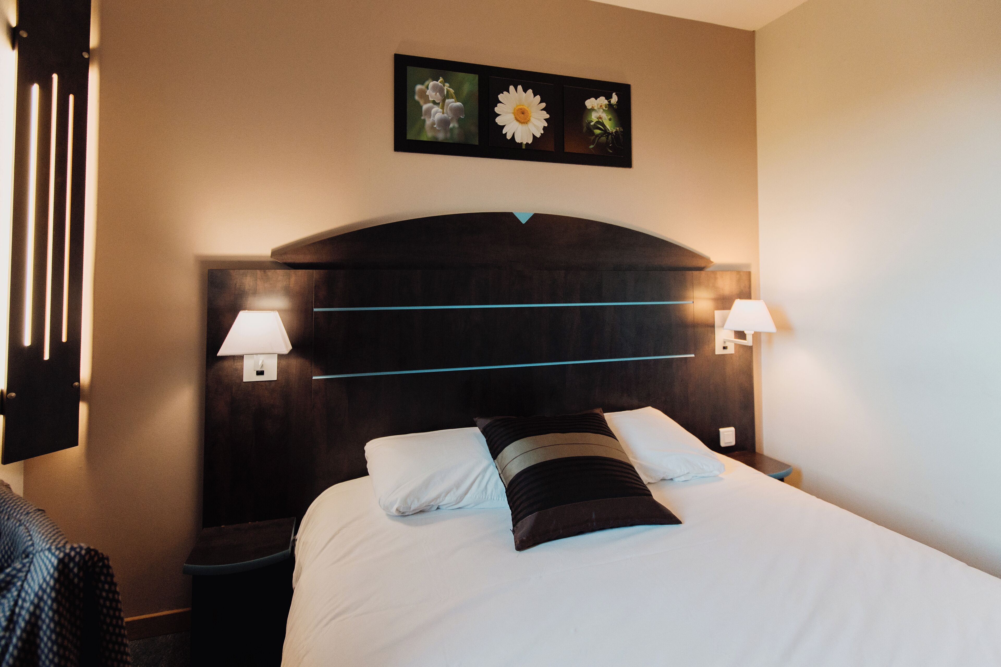 A hotel room with a large bed, two bedside lamps, a dark headboard, and a wall-mounted picture of flowers.