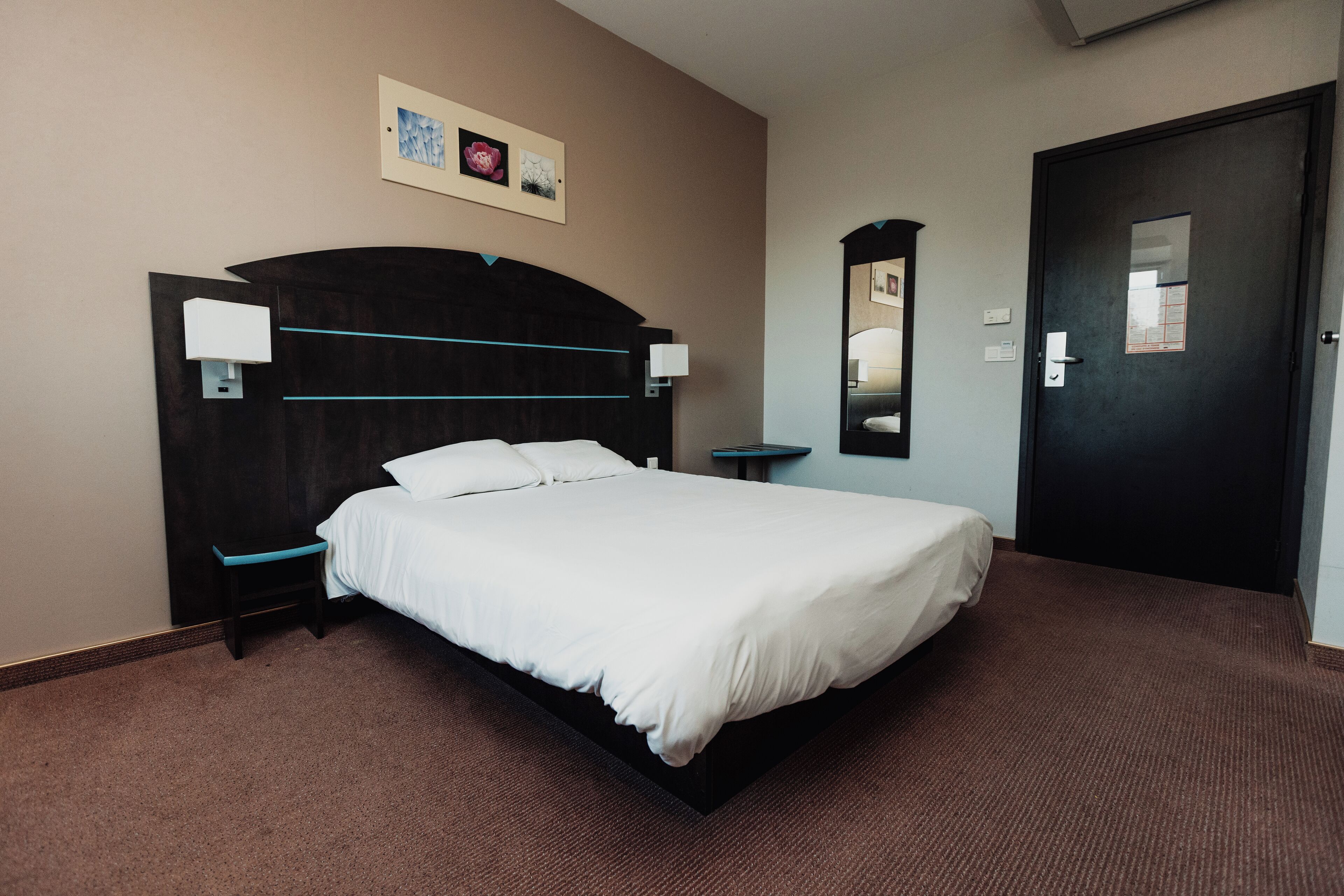 Ett hotellrum med en säng, sängbord, ett litet bord, en spegel och en dörr.