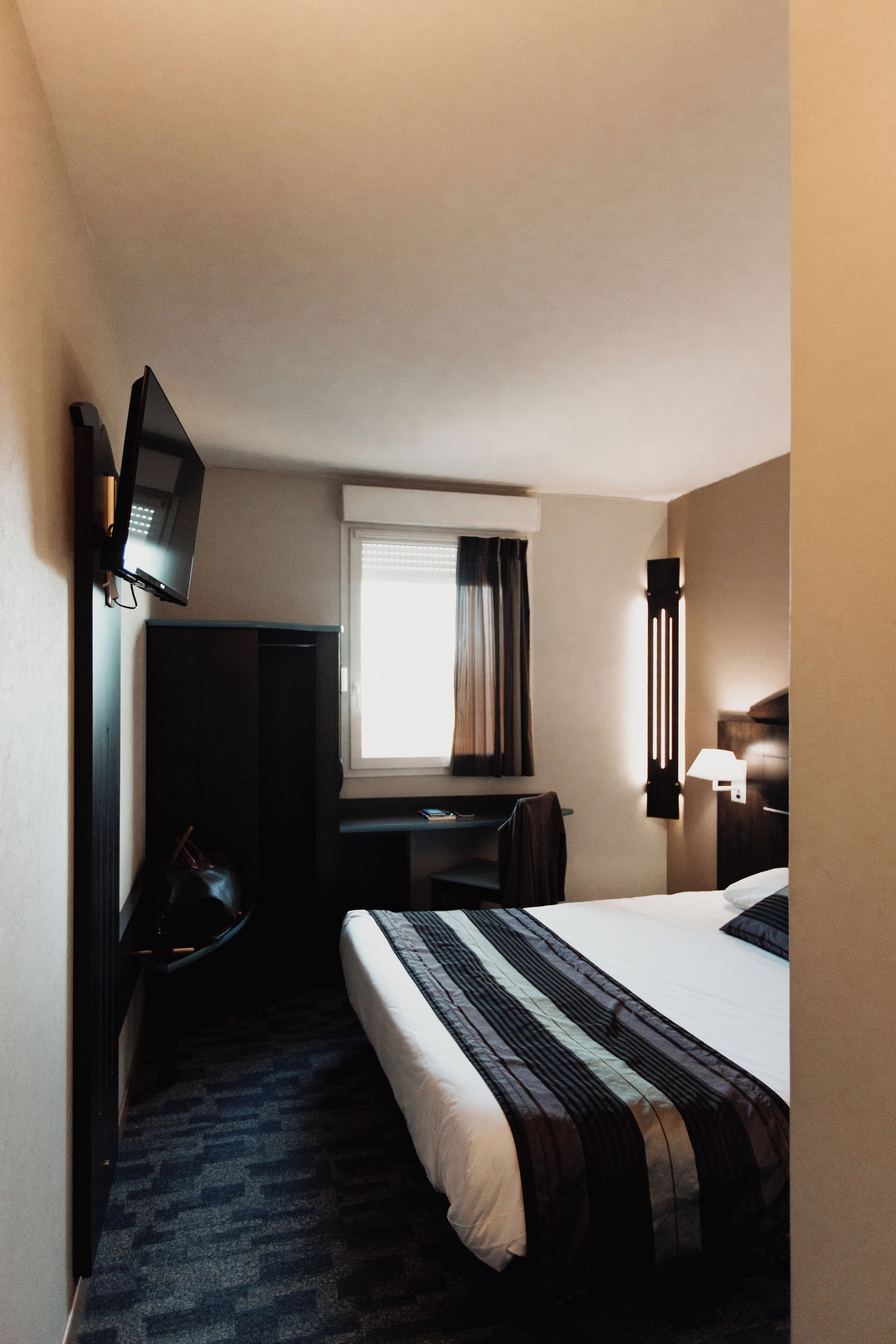 A hotel room with a bed, a desk, a chair, a television, and a window with curtains.