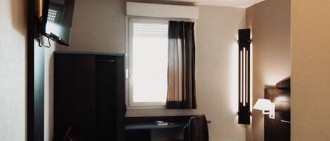 A hotel room with a bed, a desk, a chair, a television, and a window with curtains.