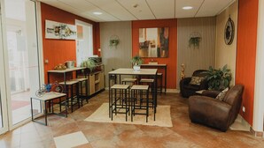 Una sala de estar moderna con comedor, un sofá y una mesa de centro. Hay varias sillas y una mesita. La habitación tiene un ventanal y una puerta.