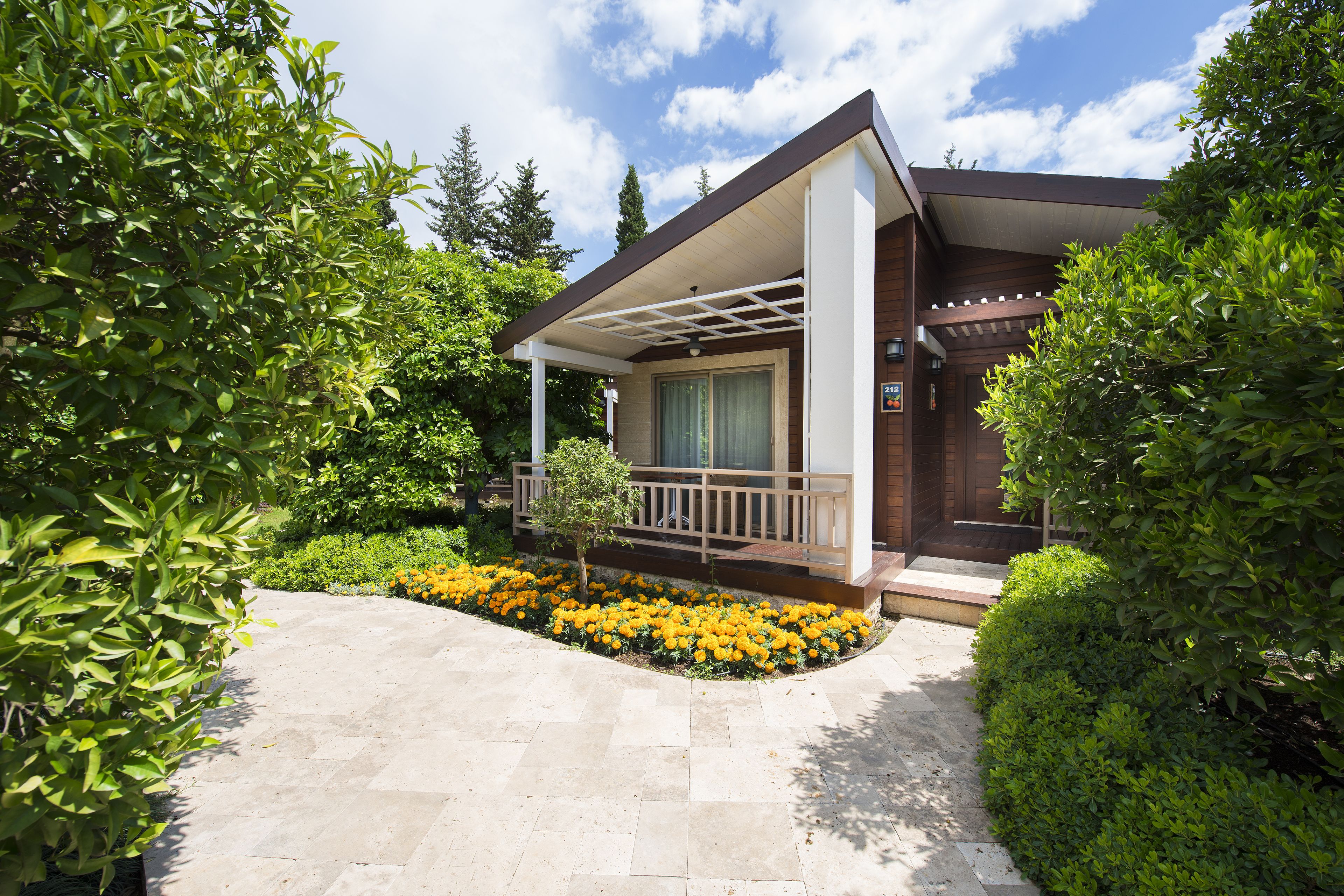 A modern house with a covered porch, a stone pathway, and a garden with yellow flowers.