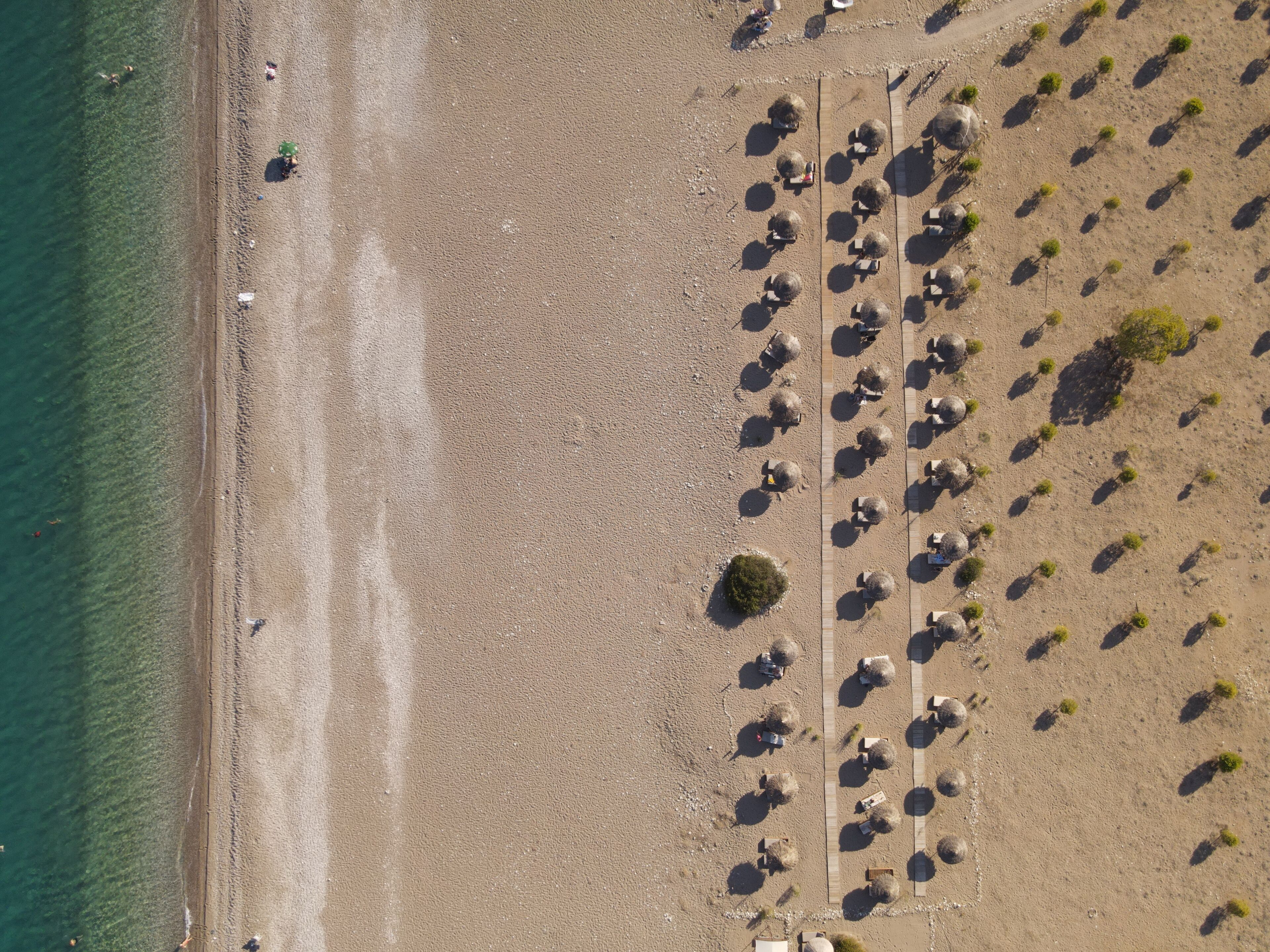 An aerial view of a beach with rows of umbrellas and beach chairs, a sandy shore, and a clear blue sea.