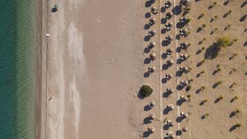 An aerial view of a beach with rows of umbrellas and beach chairs, a sandy shore, and a clear blue sea.