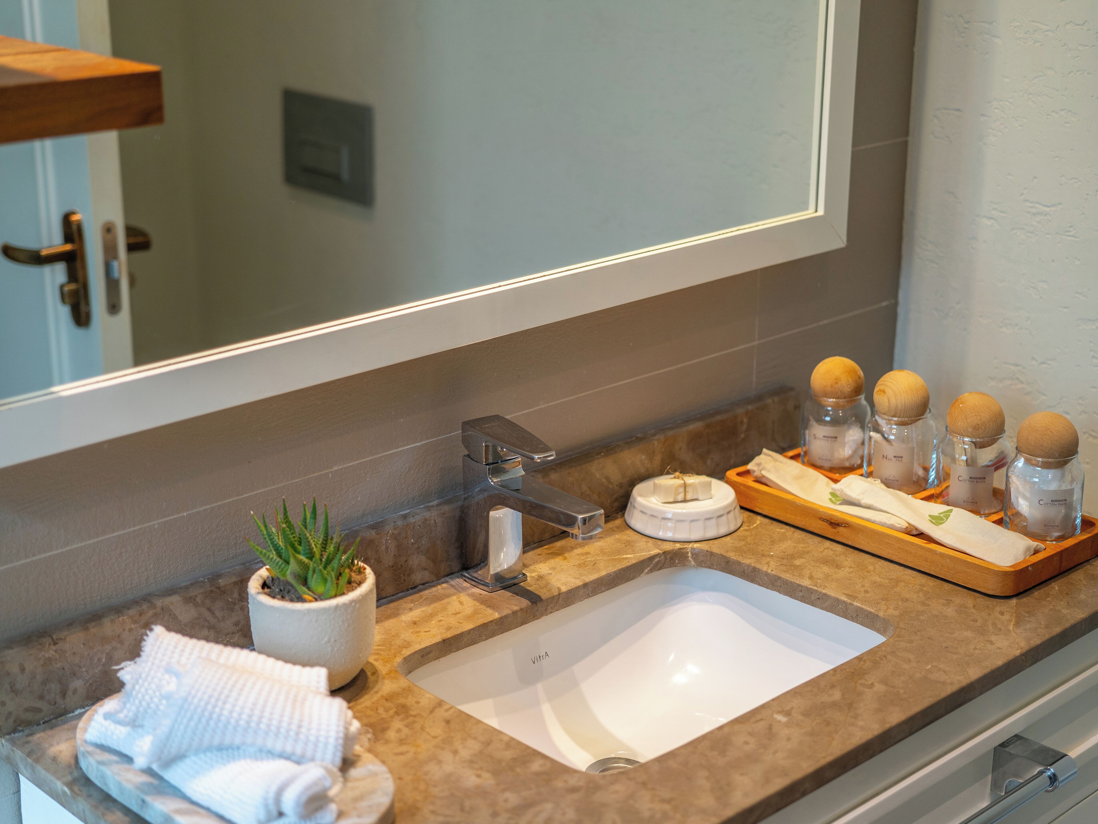 A bathroom with a white sink, a mirror, a potted plant, and a tray with jars.