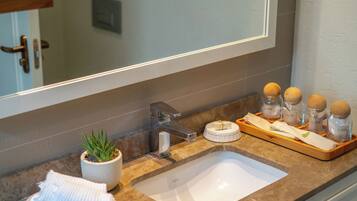 A bathroom with a white sink, a mirror, a potted plant, and a tray with jars.